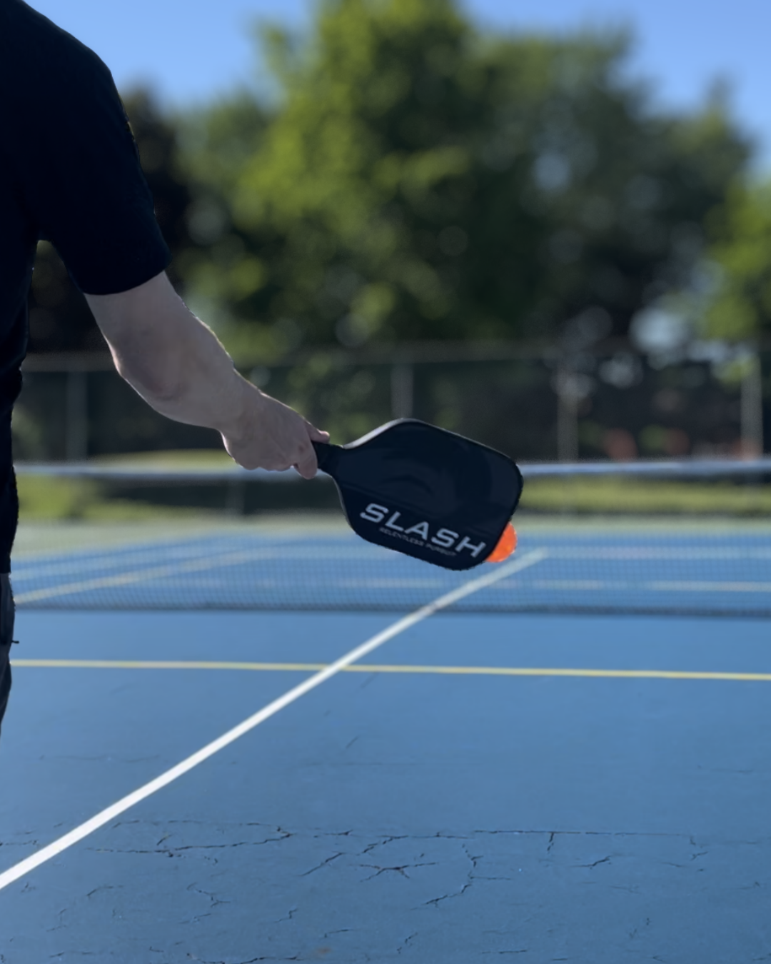 Player holding a Slash paddle in a serving stance on a blue outdoor pickleball court